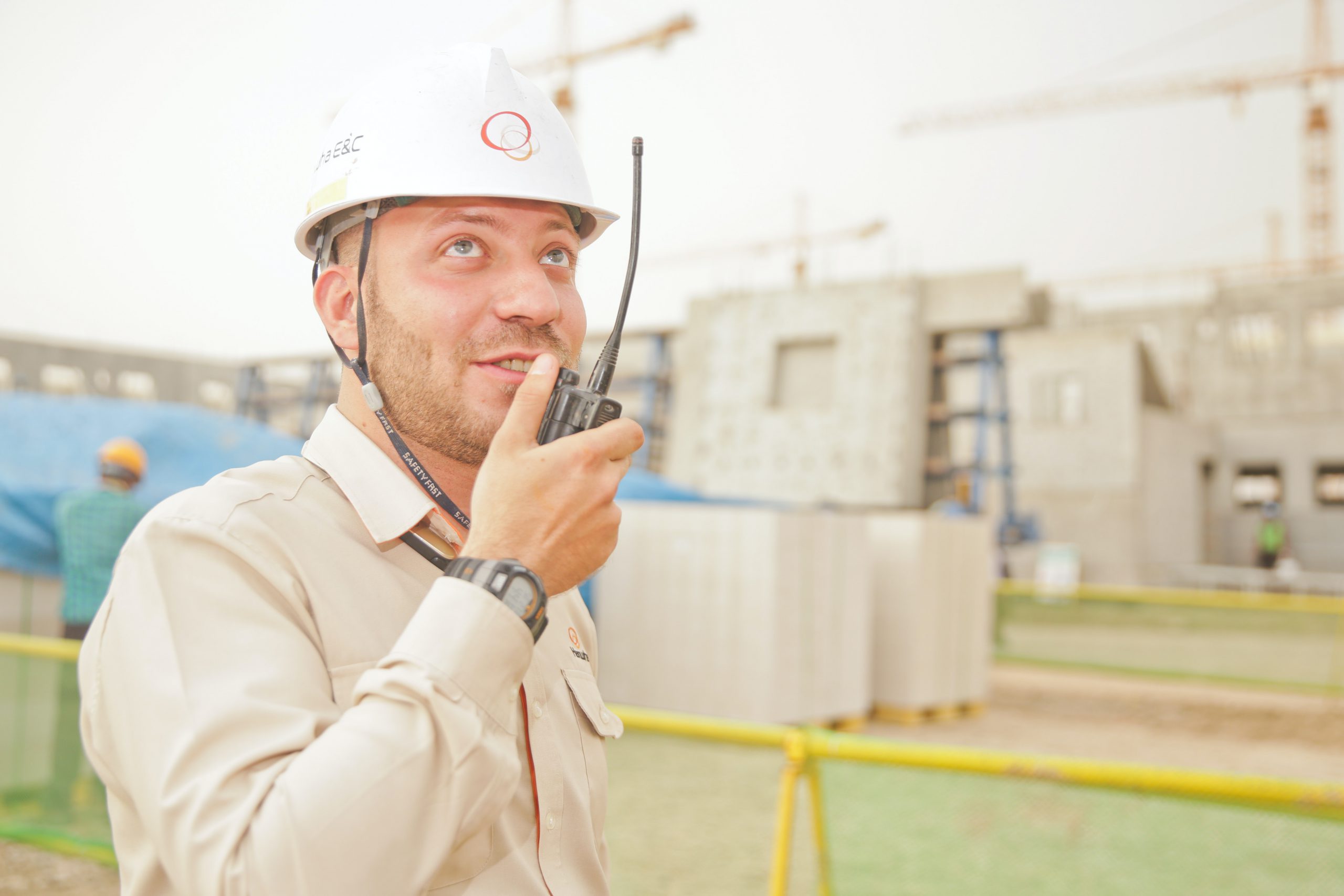 Project manager wearing a hardhat talking into handheld radio while looking onto a project.
